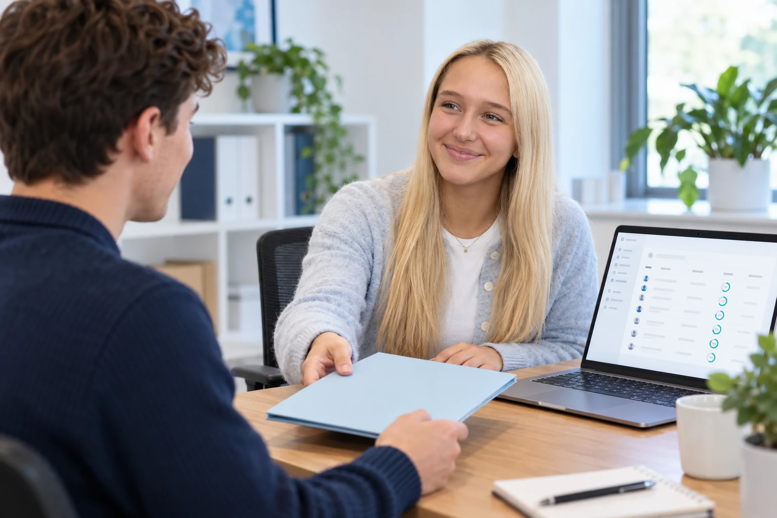Carys welcoming a new starter beside a laptop showing an onboarding overview.