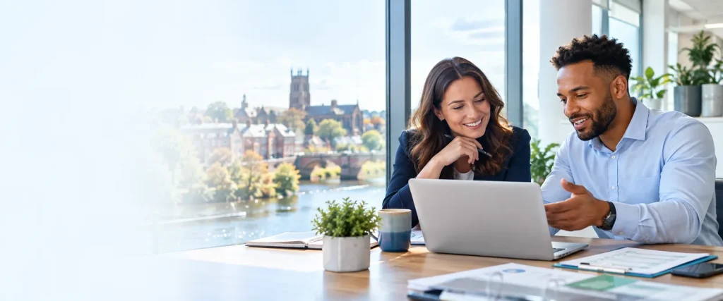 Two colleagues using a laptop beside a window overlooking a city and river